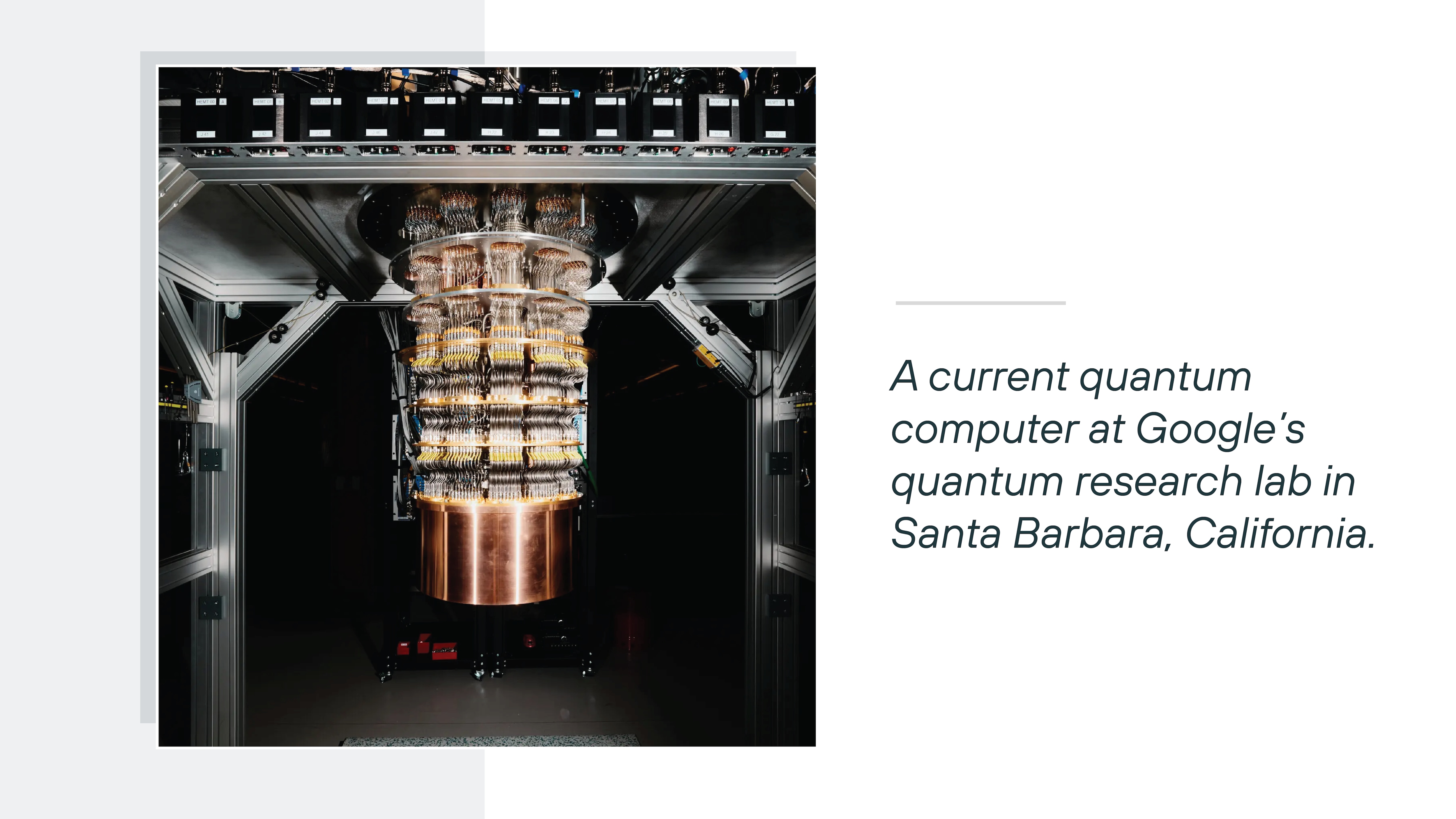 A large, vertically suspended quantum computing apparatus hangs at the center of a metallic laboratory frame, with multiple stacked circular tiers made of copper and gold-colored components connected by intricate wiring and cooling structures. The surrounding environment is dim, with structural beams, cables, and equipment framing the system. To the right, dark green text on a white background reads 'A current quantum computer at Google's quantum research lab in Santa Barbara, California.'